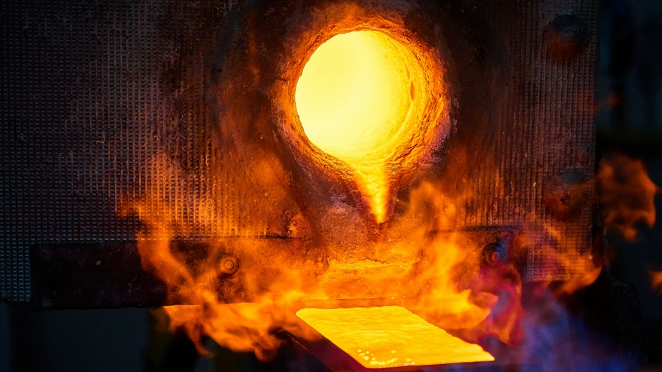 Filling graphite casting form with hot melted gold metal in shielding gases sphere in production plant.